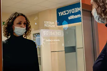 Dziewczyna stoi przed lustrem reklamowym na korytarzu Centrum Medycznego MEDYK